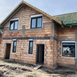 WINDOBEST SP. Z O.O - Surowy budynek z cegły z zamontowanymi, czarnymi oknami i przygotowanym dachem, w trakcie budowy, z widocznymi detalami konstrukcyjnymi.