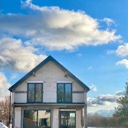 WINDOBEST SP. Z O.O - Dom w stanie surowym otwartym, z zamontowanymi oknami na dwóch kondygnacjach, na tle błękitnego nieba z chmurami.