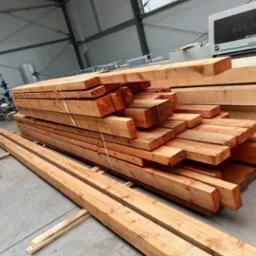 Stos belek drewnianych ułożonych w magazynie, widoczne ślady cięcia i pomarańczowe oznaczenia na końcach.