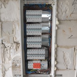ELPRO Piotr Pisaniak - Rozdzielnica elektryczna Hager zamontowana na surowej ścianie z widocznymi przewodami, zabezpieczeniami i pianką montażową.