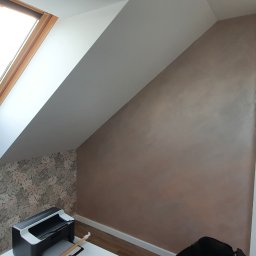 Michał Kulesza - Poddasze po remoncie: ściana z efektem dekoracyjnym w odcieniach brązu, sąsiadująca ze ścianą pokrytą tapetą w liście, okno dachowe w drewnianej ramie.