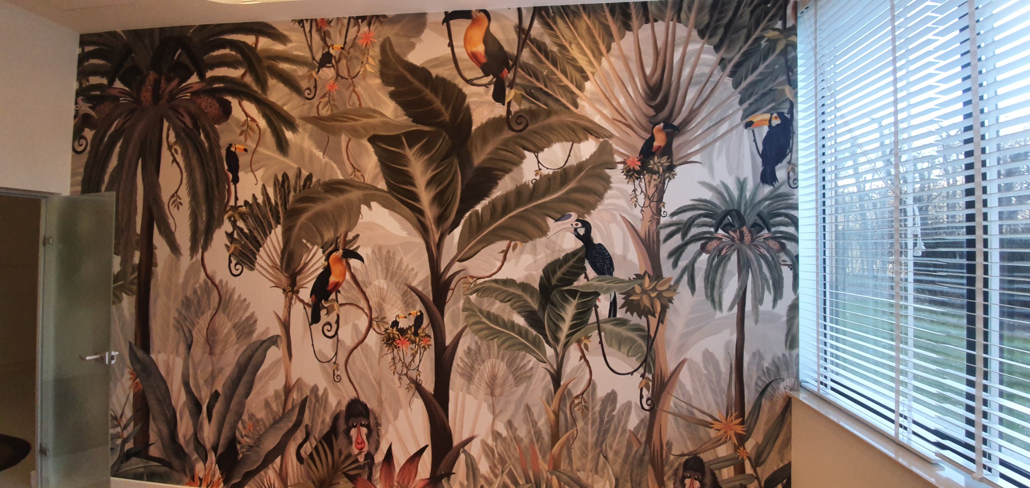 Ściana pokryta tapetą z motywem dżungli: tukany, małpy i roślinność tropikalna, widok z perspektywy pokoju z żaluzjami.