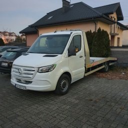 Oscar Kamil Osinski - Biała laweta Mercedes-Benz Sprinter zaparkowana na brukowanym podjeździe przed domem z ciemną dachówką, widoczny numer rejestracyjny.