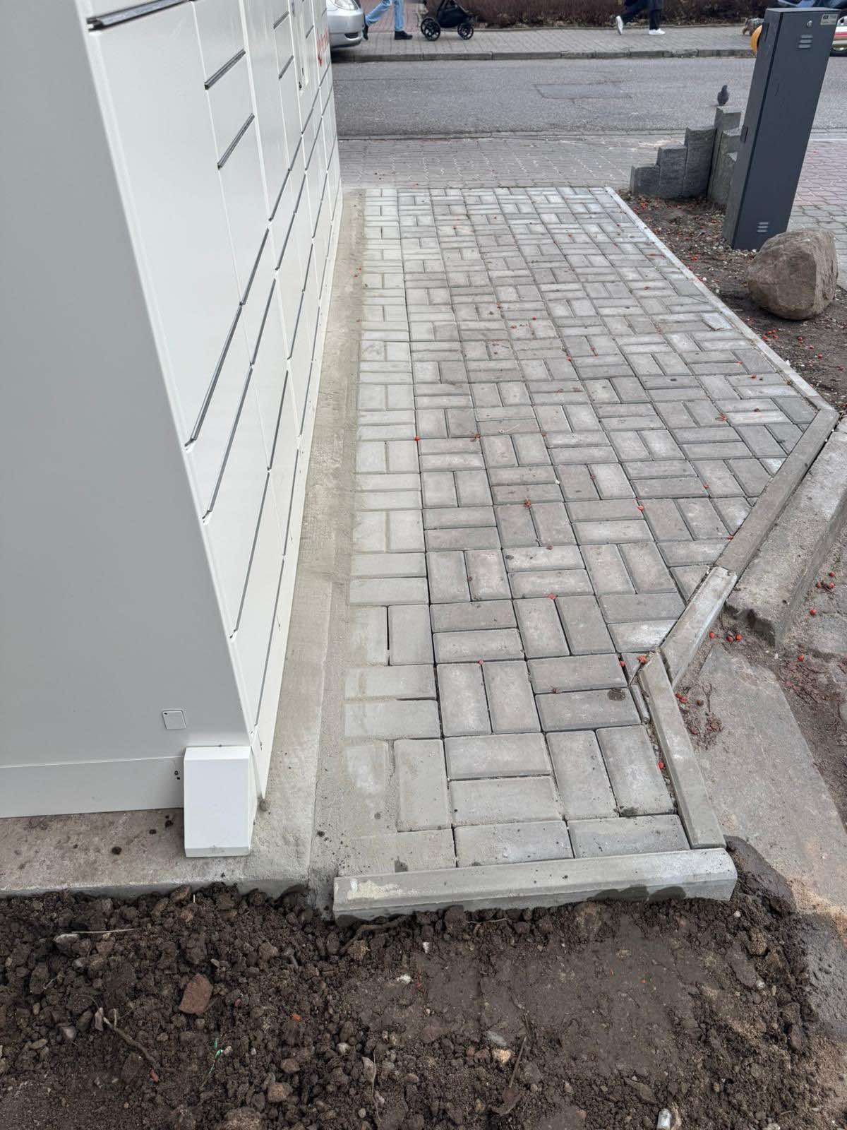 Ułożona kostka brukowa przy paczkomacie, widoczne świeże ślady po cięciu kostki i ziemia.