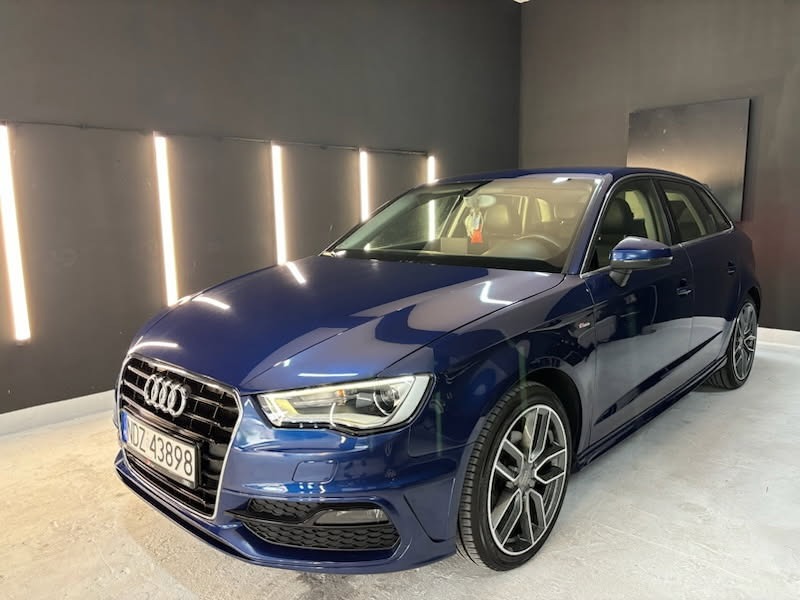 Błyszczący, granatowy Audi A3 po detailingu. Widoczne odbicie światła na lakierze, felgi aluminiowe. Tablica rejestracyjna widoczna.