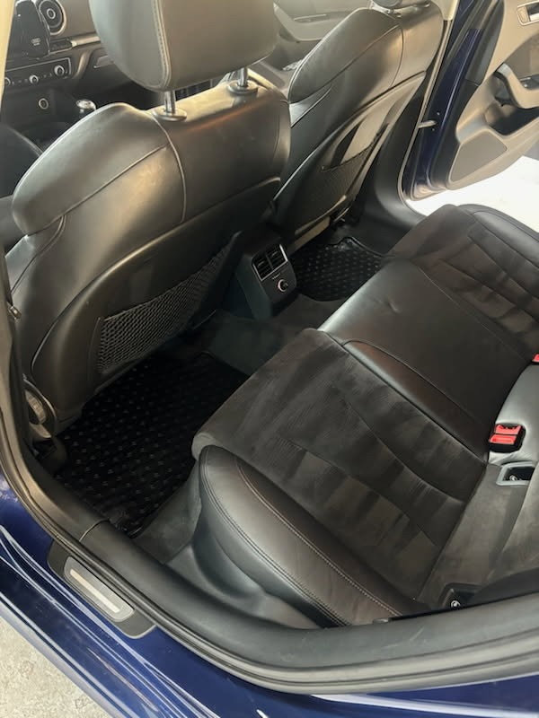 Wnętrze samochodu z czarnymi skórzanymi siedzeniami i gumowymi dywanikami. Widoczne tylne siedzenia i fragment przednich foteli. Auto w kolorze ciemnego granatu.