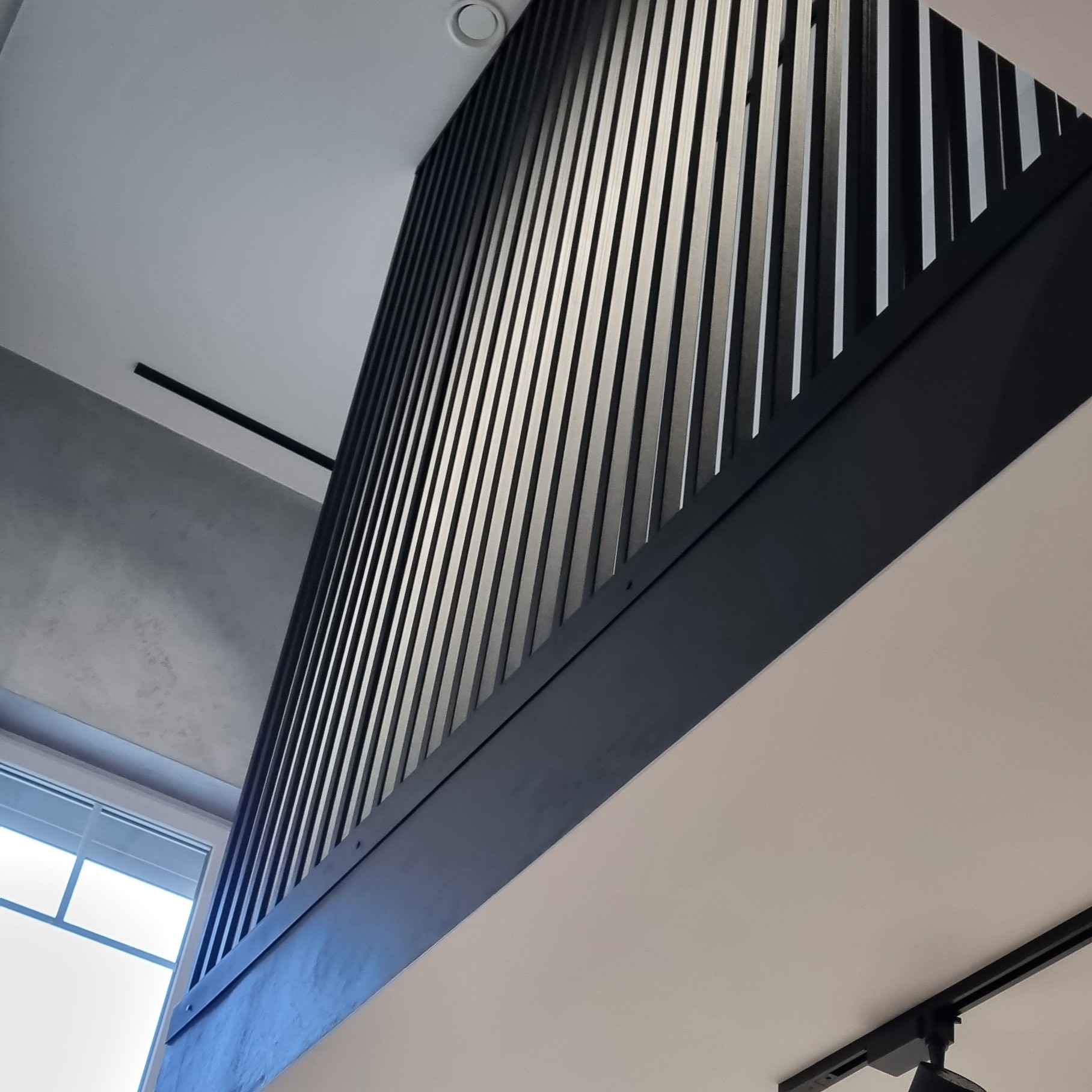 Nowoczesna balustrada metalowa schodów z pionowymi szczeblami w kolorze czarnym, widok od dołu, z oświetleniem sufitowym.