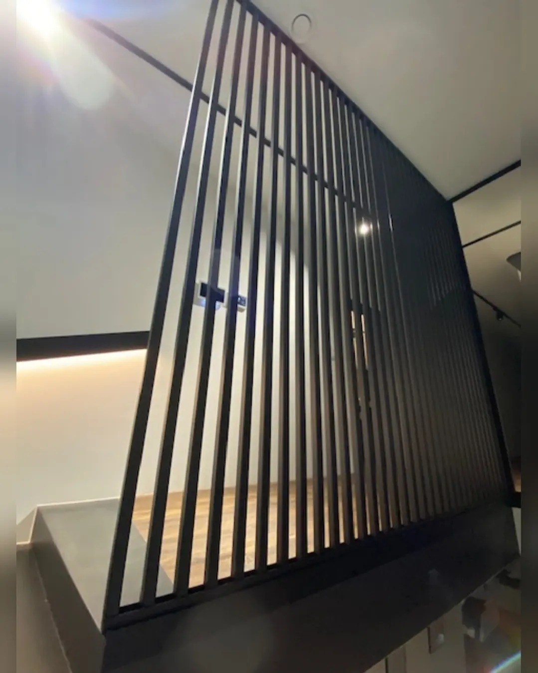 Nowoczesna balustrada schodowa z pionowych, czarnych metalowych prętów, widok z dołu, oświetlenie sufitowe.