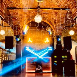 DJ BASMAN Marcin Kowalczyk - Oświetlenie eventowe w ceglanym wnętrzu z parkietem: reflektory, kule dyskotekowe i dekoracyjne światełka tworzą klimat imprezy. DJ'ka z napisem 'Let's Dance!'.