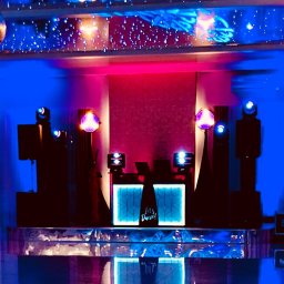 DJ BASMAN Marcin Kowalczyk - Scena DJ-a z podświetlanym panelem 'Let's Dance!', głośnikami i efektami świetlnymi w odcieniach niebieskiego i różowego. Dekoracja sufitu imituje gwiazdy.