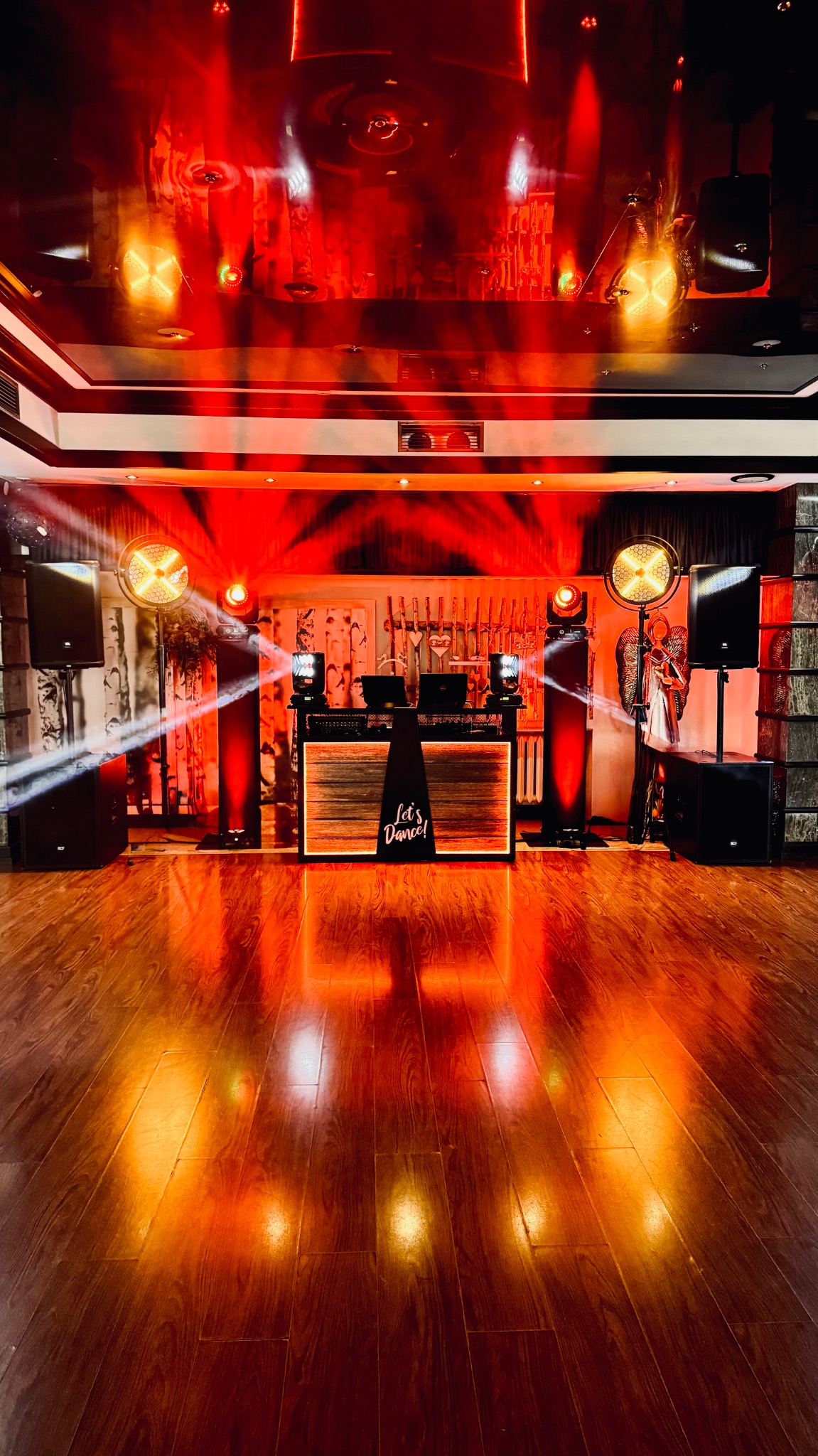 Scena z nagłośnieniem i oświetleniem w czerwonej tonacji, parkiet odbija światło. Na podeście konsola DJ-ska z napisem 'Let's Dance!'.