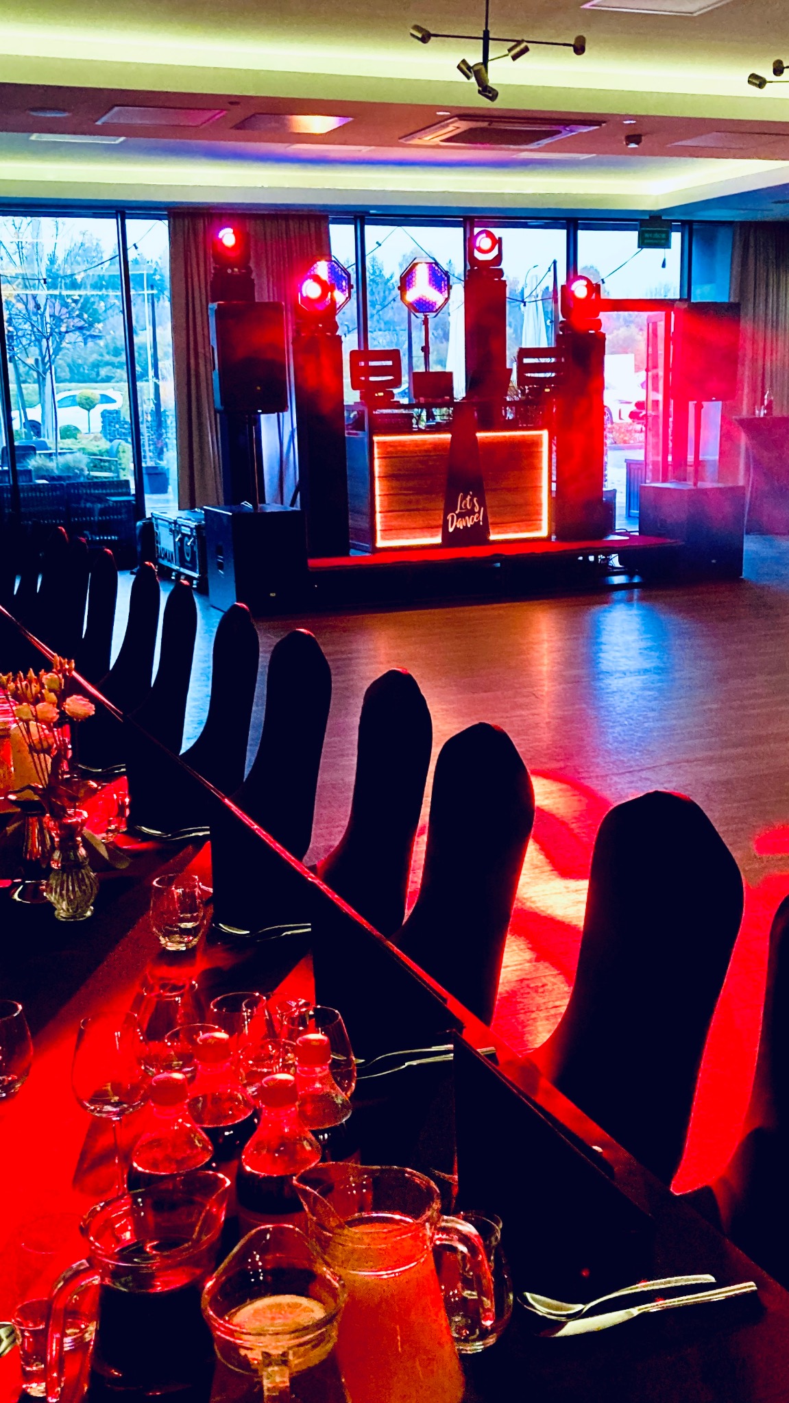 Sala bankietowa z oświetleniem scenicznym i stołami nakrytymi do przyjęcia. Scena z napisem 'Let's Dance' w tle. Ujęcie z perspektywy stołu.