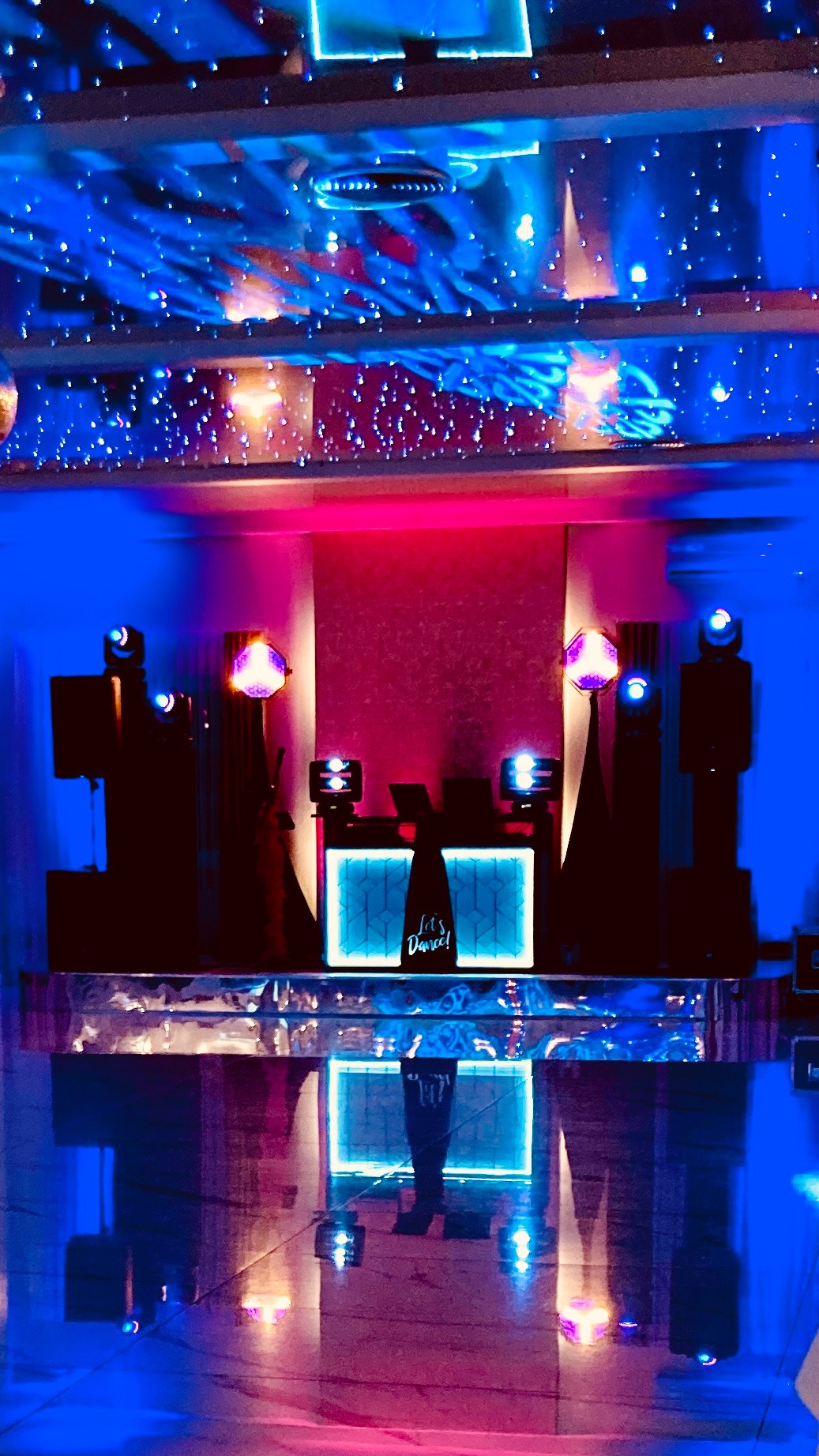 Scena DJ-a z podświetlanym panelem 'Let's Dance!', głośnikami i efektami świetlnymi w odcieniach niebieskiego i różowego. Dekoracja sufitu imituje gwiazdy.