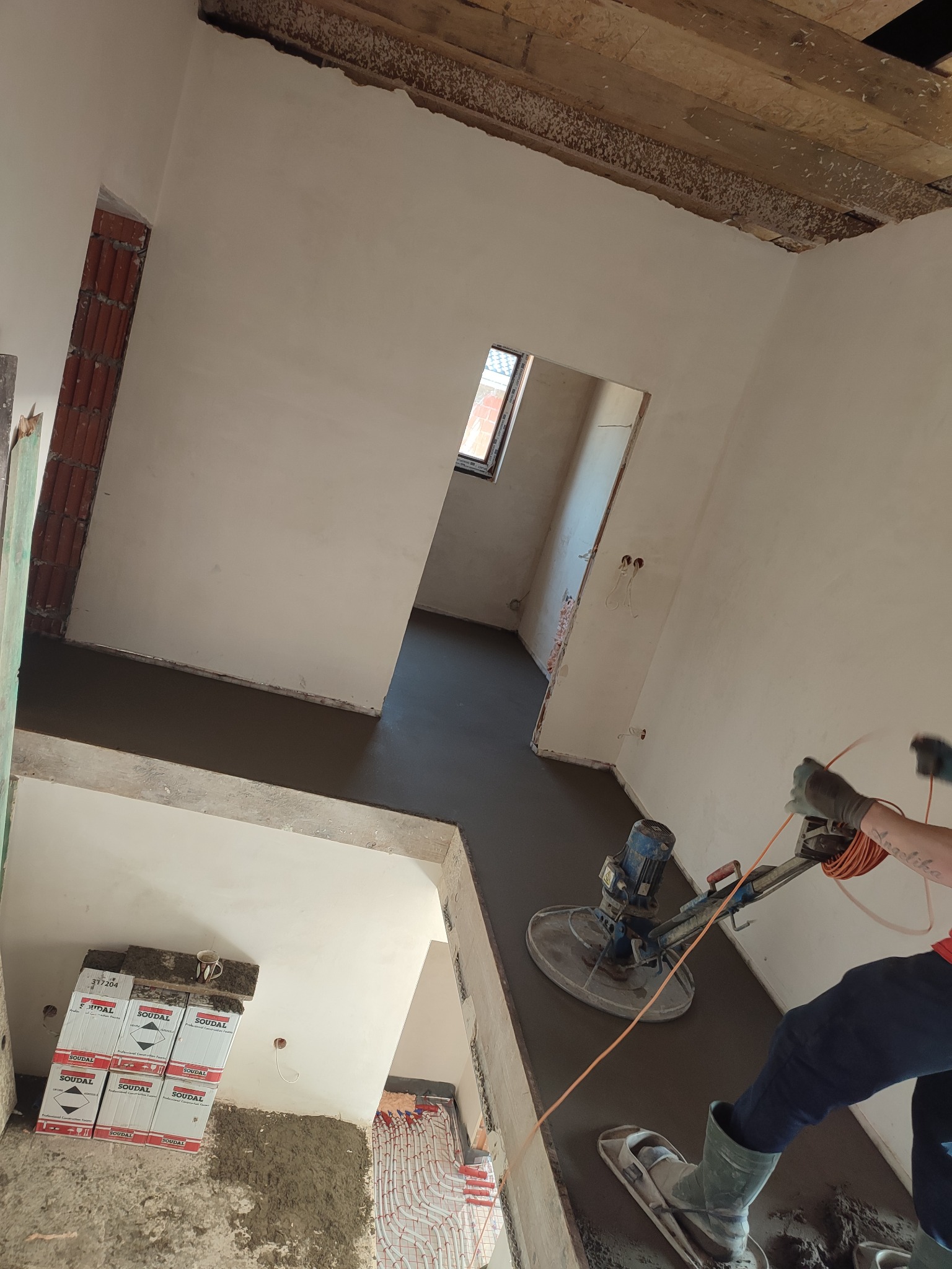 Prace wykończeniowe: Szlifowanie wylewki jastrychowej za pomocą zacieraczki mechanicznej w pomieszczeniu z instalacją ogrzewania podłogowego i przygotowanymi ścianami.