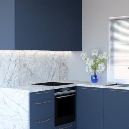 HAD Project - Nowoczesna, narożna kuchnia w odcieniach granatu i bieli, z marmurowym blatem i backsplash'em podświetlonym listwą LED, uzupełniona niebieskim wazonem z białymi kwiatami na blacie.