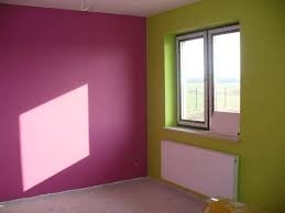 Pomalowane wnętrze pokoju: ściana w odcieniu fuksji z wyraźnym kwadratowym cieniem, sąsiadująca ze ścianą w kolorze limonkowym, okno z białymi ramami i grzejnikiem pod nim.