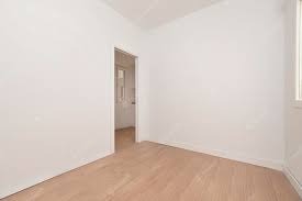 Pusty, pomalowany na biało pokój z jasnymi panelami podłogowymi i otwartymi drzwiami do kolejnego pomieszczenia.