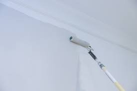 Wałek malarski z długą rączką w trakcie pracy, świeżo pomalowana na biało ściana w Jaworze, widoczne delikatne smugi farby.