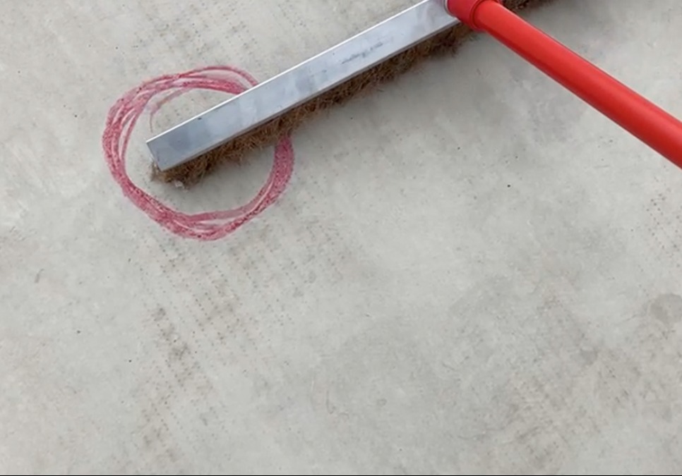 Szczotka dekarska z czerwoną rączką, pozostawiająca ślad w kształcie okręgu na jasnej powierzchni dachu.