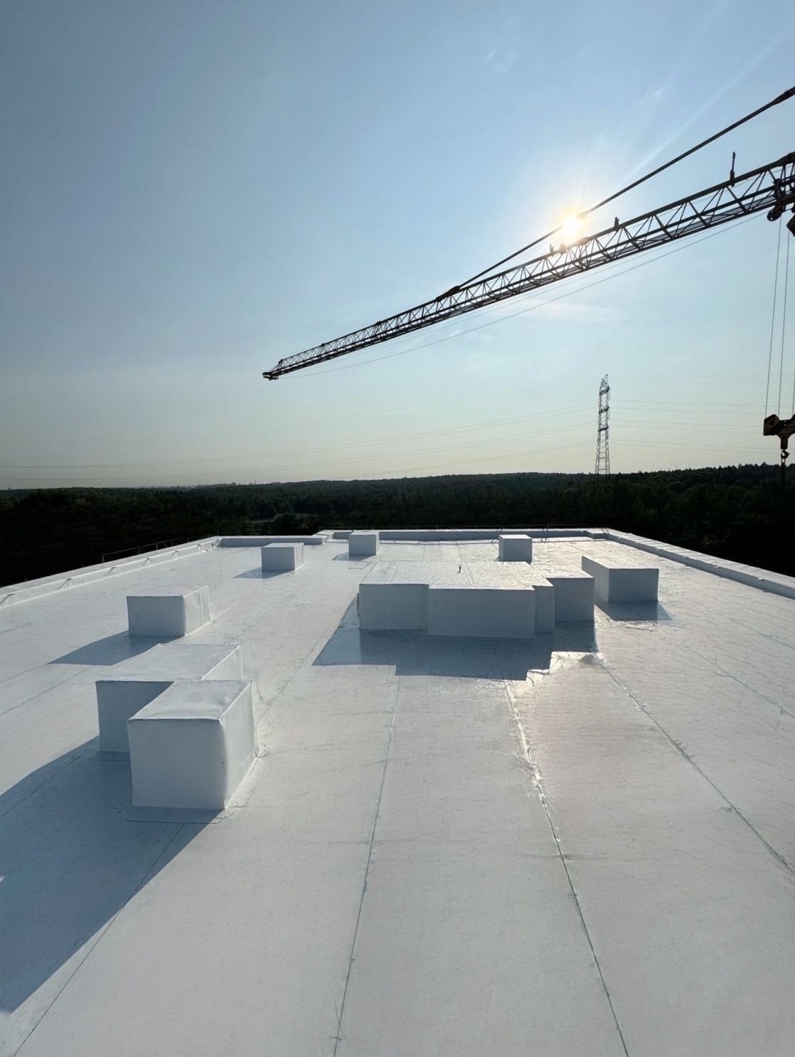 Białe, płaskie pokrycie dachu budynku w Warszawie z widocznymi kominkami wentylacyjnymi i żurawiem budowlanym w tle, wykonane w technologii hydroizolacji.