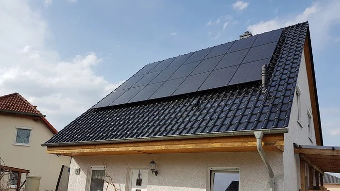 Dom jednorodzinny w Lublinie z zainstalowanymi panelami słonecznymi na czarnym, ceramicznym dachu. Widoczne okno, lampa zewnętrzna i białe drzwi wejściowe.