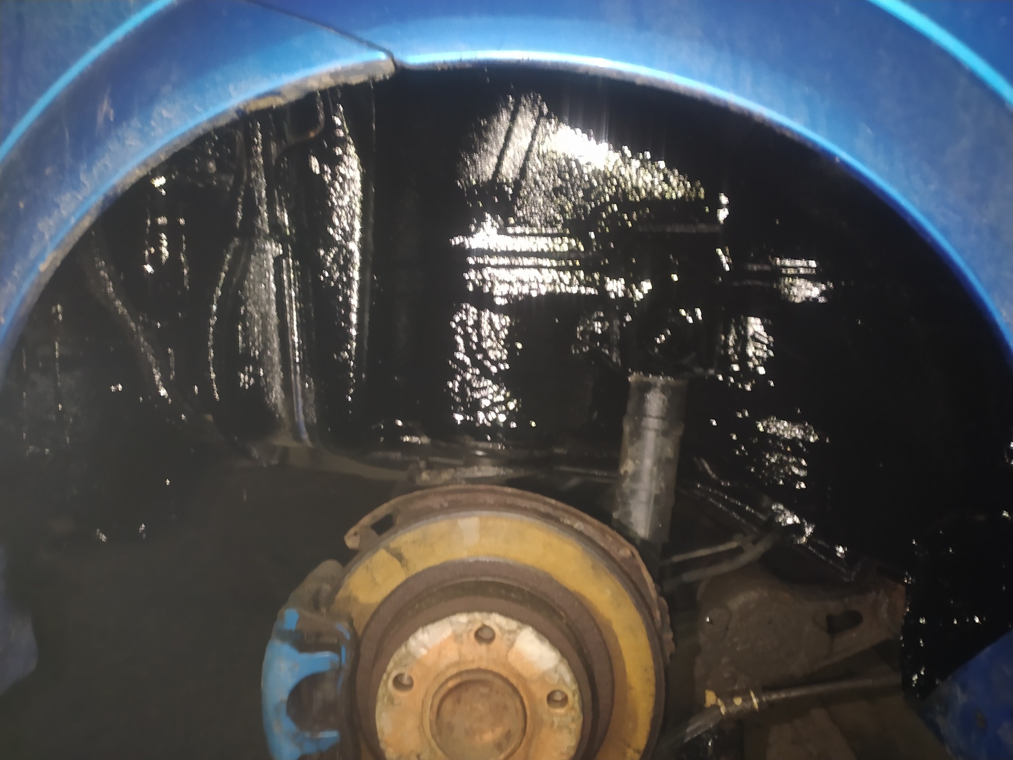 Błotnik niebieskiego samochodu po zabezpieczeniu antykorozyjnym, widoczna gruba, błyszcząca warstwa ochronna.