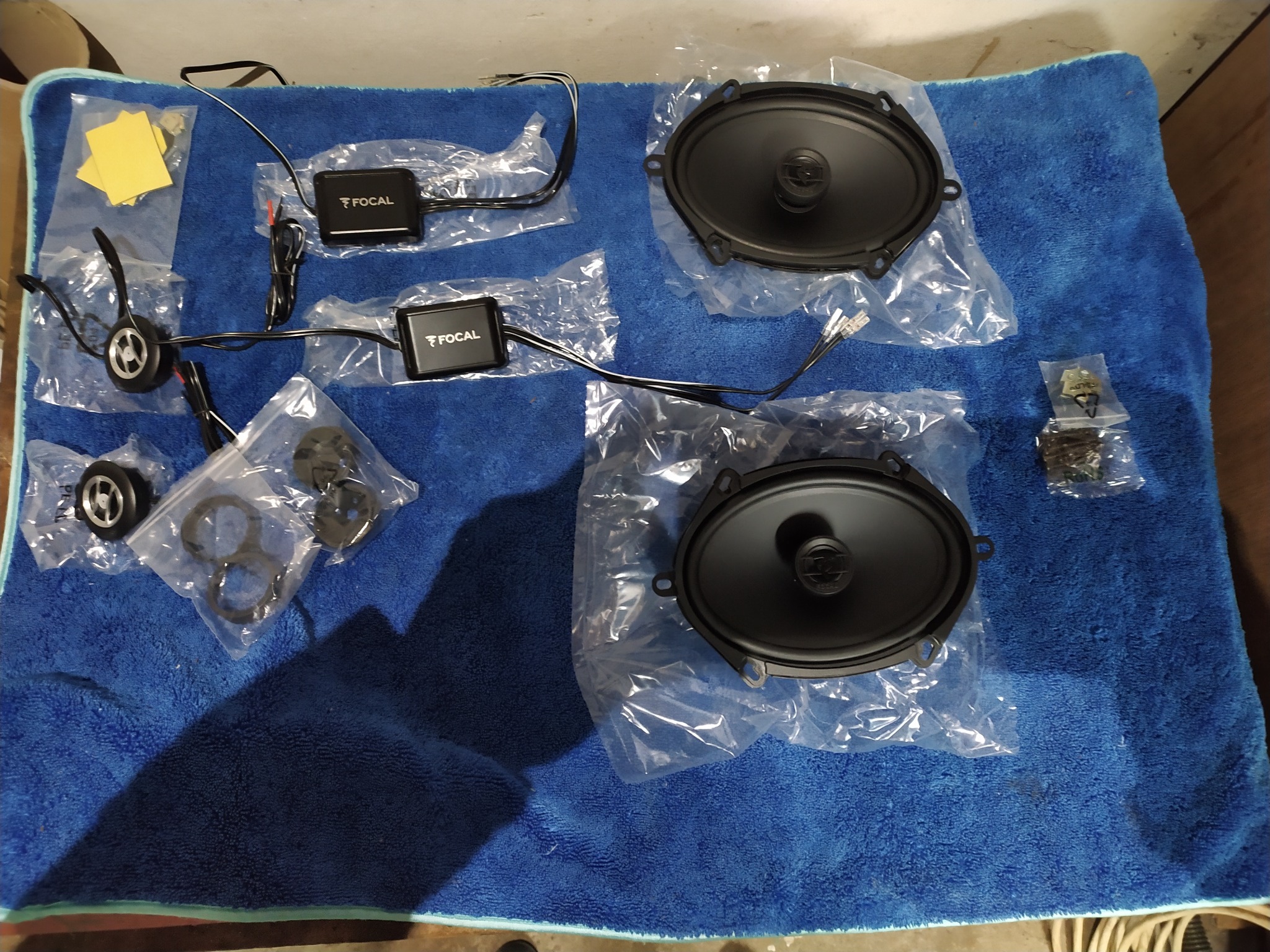Zestaw głośników samochodowych Focal, zwrotnice, tweetery i akcesoria montażowe rozłożone na niebieskim ręczniku frotte.