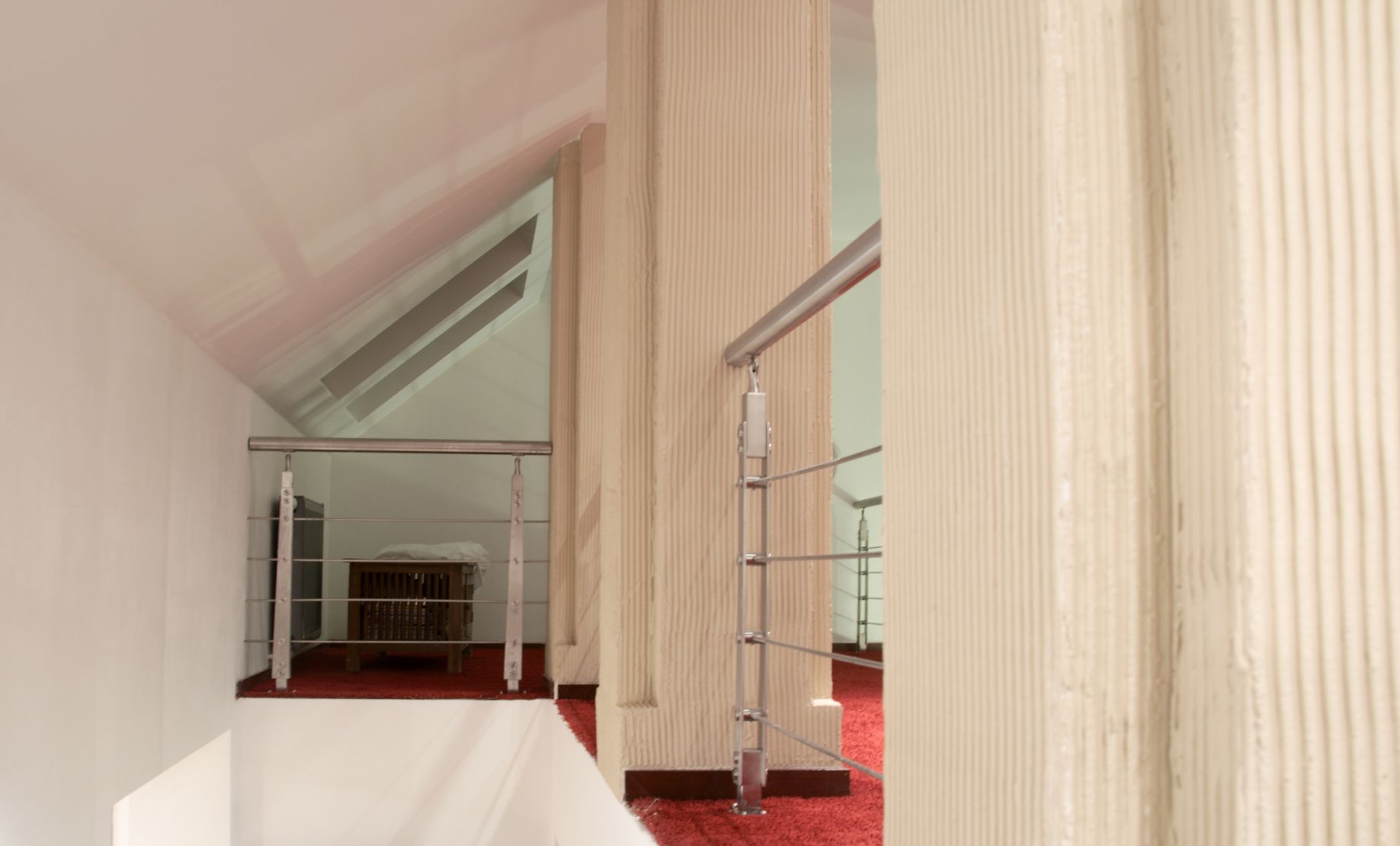 Klatka schodowa w domu z czerwonym dywanem i kolumnami wykończonymi dekoracyjną strukturą, widok z góry.