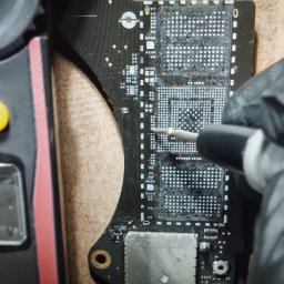 Fix Lab Center sp. z o.o. - Naprawa płyty głównej: precyzyjne lutowanie układu BGA pod mikroskopem, z użyciem multimetru do pomiaru napięcia. Czarny laminat, białe punkty lutownicze.