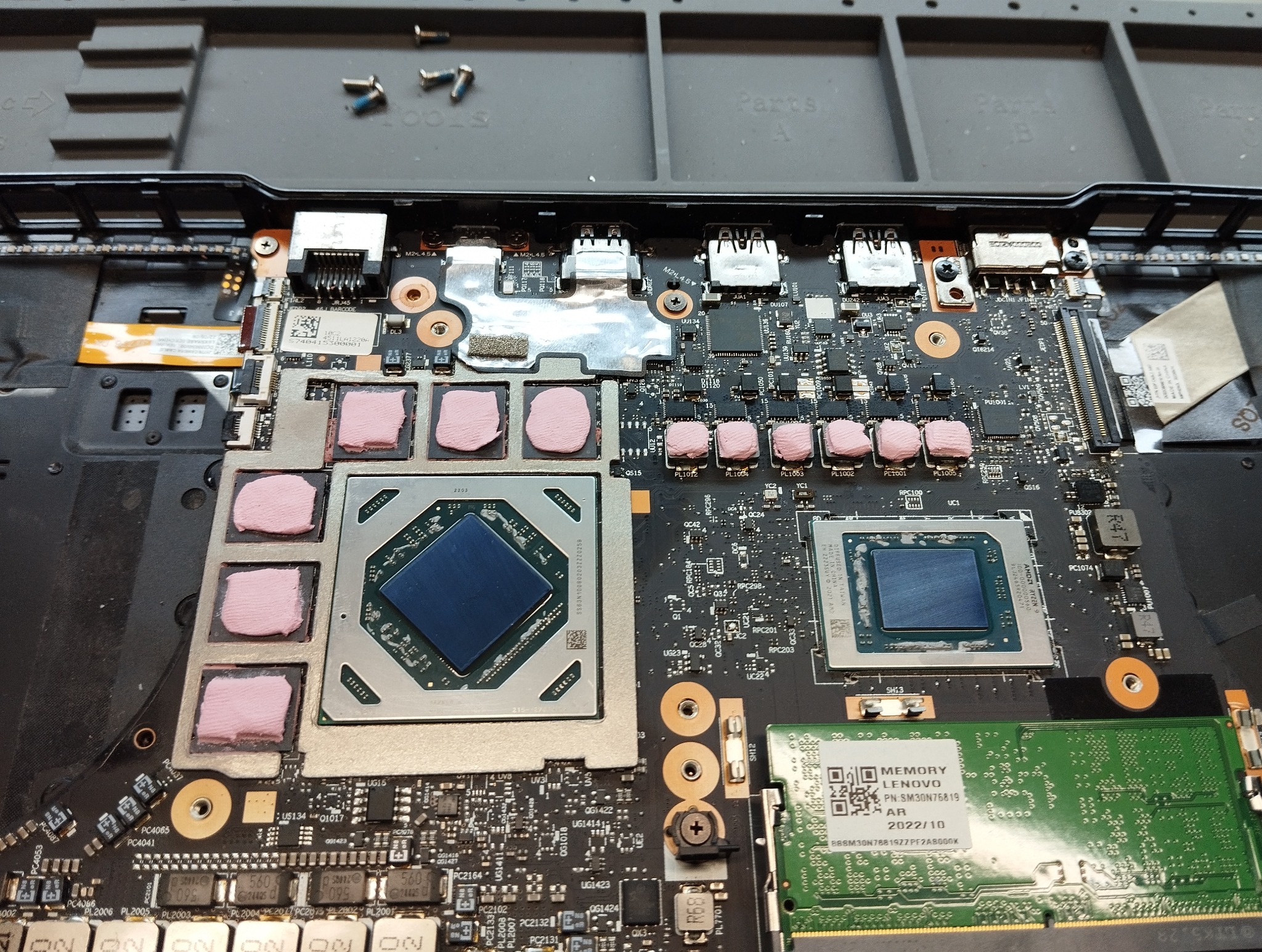 Otwarty laptop z widoczną płytą główną, procesorami z nałożonymi termopadami i modułem pamięci RAM Lenovo. Widoczne śrubki i narzędzia na macie serwisowej.