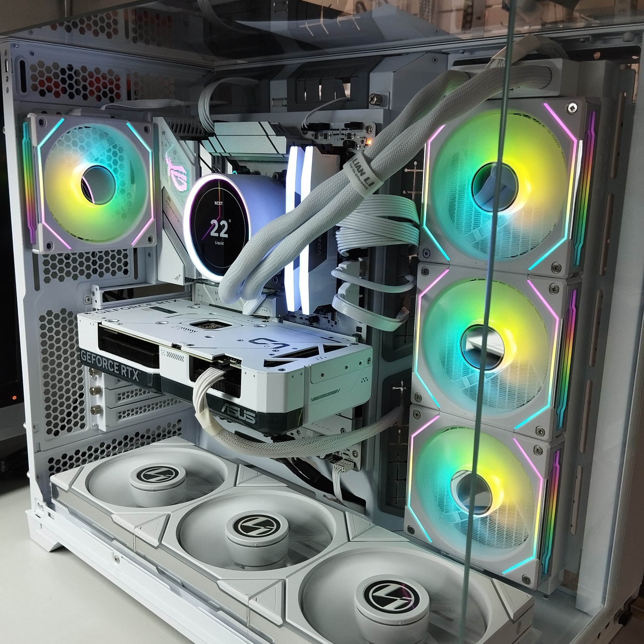 Biała obudowa komputera PC z podświetleniem RGB, chłodzeniem wodnym i kartą graficzną GeForce RTX. Widoczne wentylatory Lian Li i elementy Asus ROG.