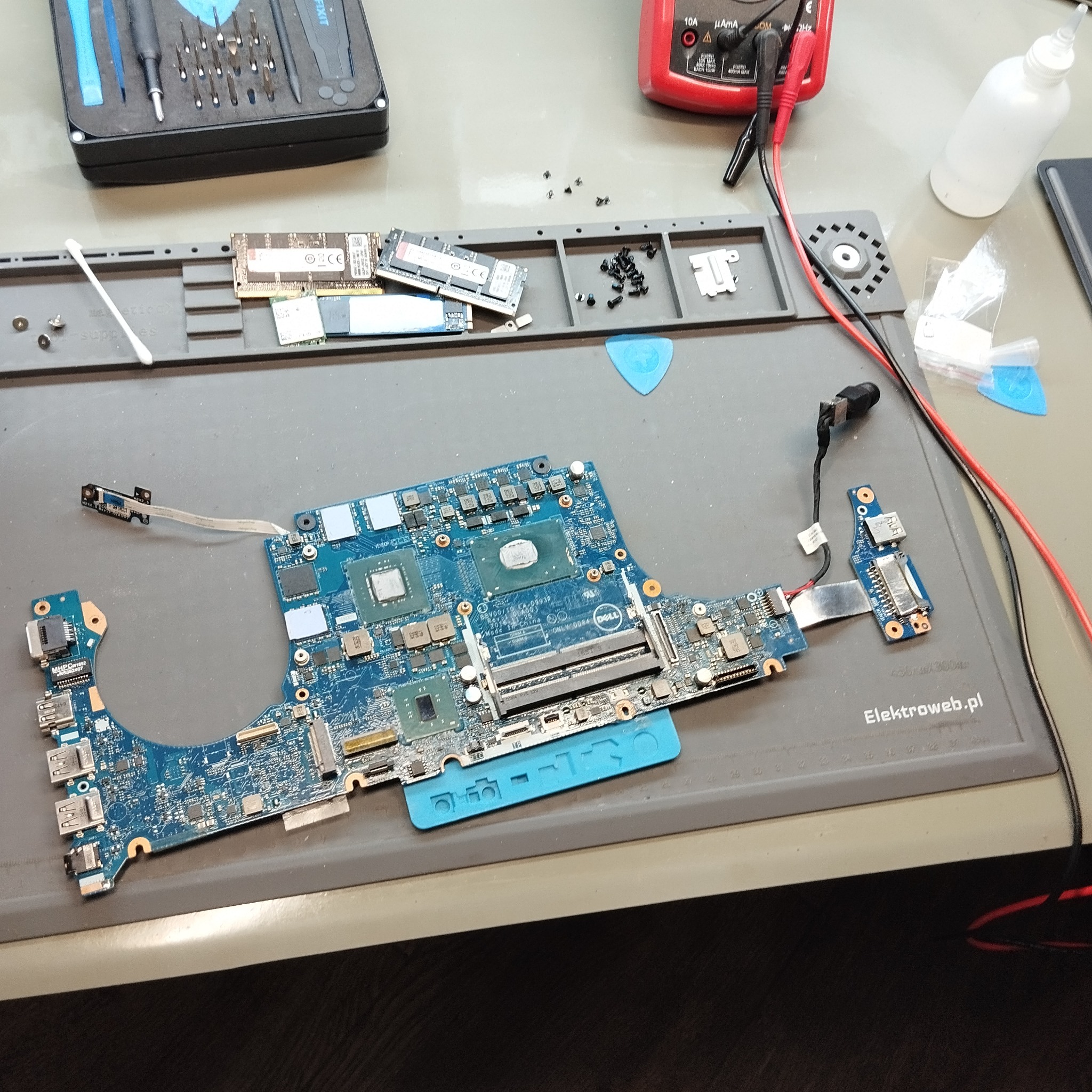 Płyta główna laptopa Dell na macie serwisowej, narzędzia, miernik, elementy komputera. Widoczny etap naprawy, serwis komputerowy.