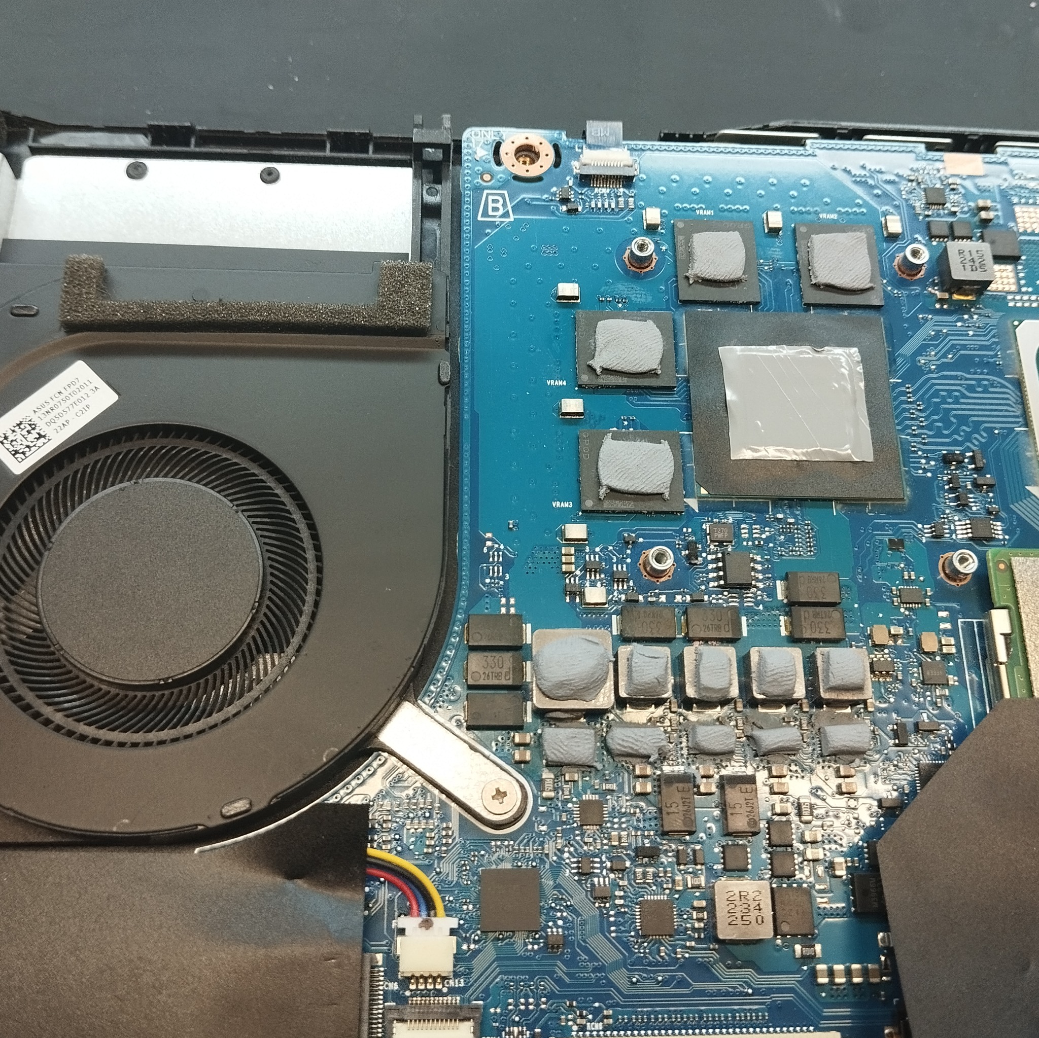 Wnętrze laptopa ASUS z widoczną płytą główną, elementami chłodzenia i układami scalonymi pokrytymi szarą pastą termoprzewodzącą. Widoczne napisy 'VRAM' i 'ASUS FCN FPD7'.