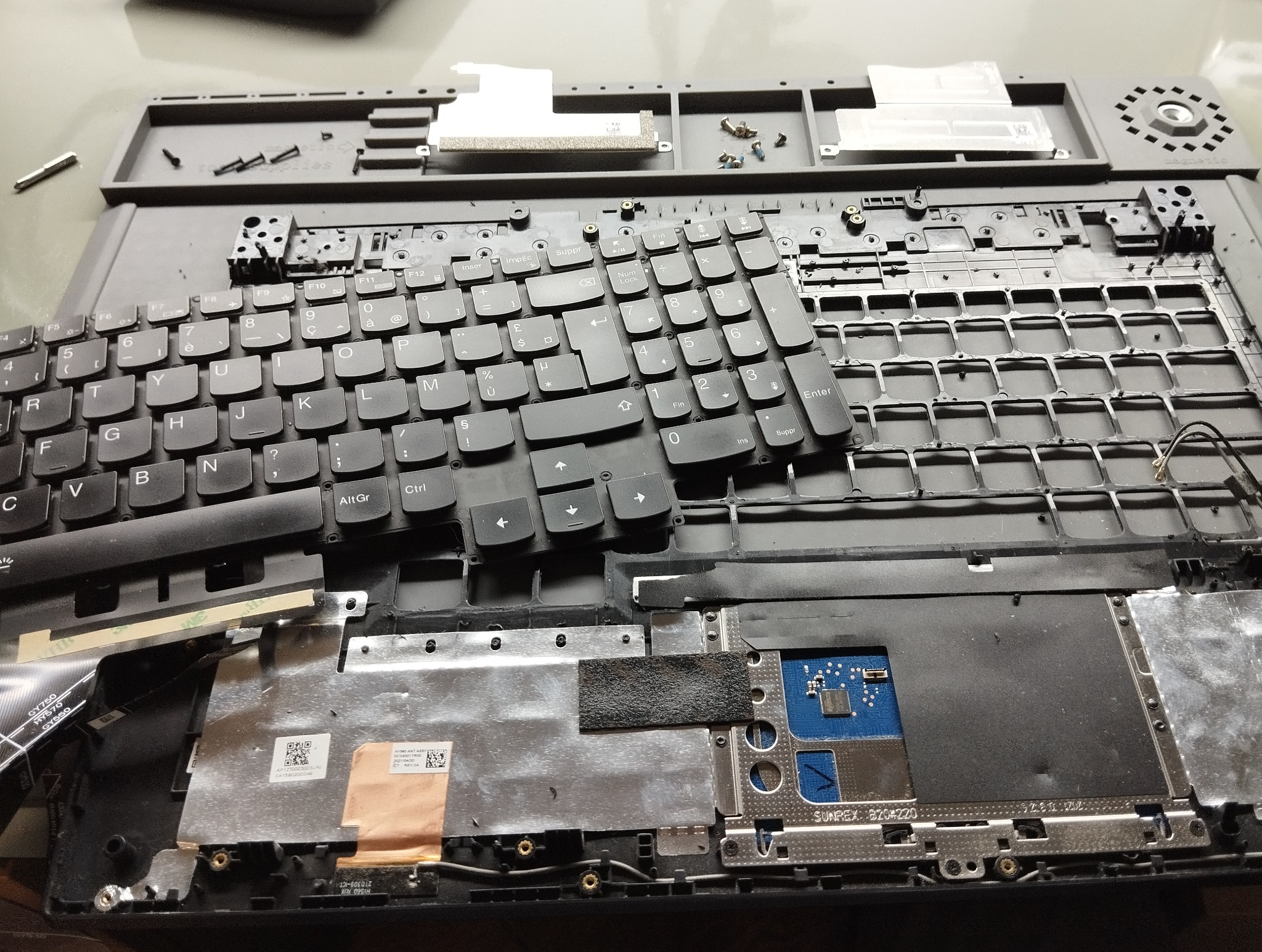 Rozłożony laptop z częściowo zdjętą klawiaturą, widoczne elementy wewnętrzne i śrubki. Układ klawiszy QWERTY. Naprawa laptopa w toku.