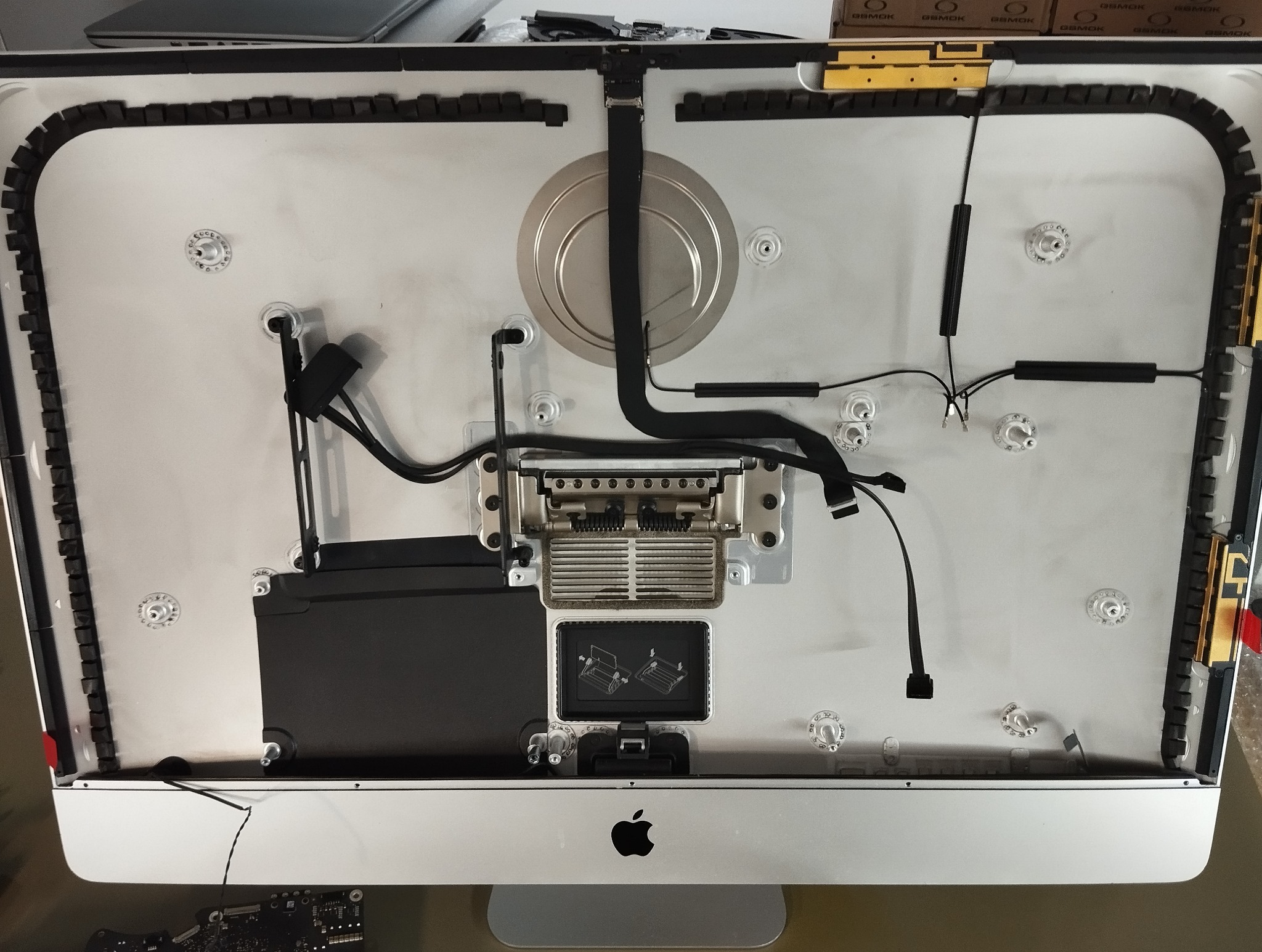 Wnętrze rozłożonego komputera iMac z widocznymi elementami elektroniki, kablami i radiatorem, ukazujące etap naprawy lub serwisu sprzętu komputerowego.