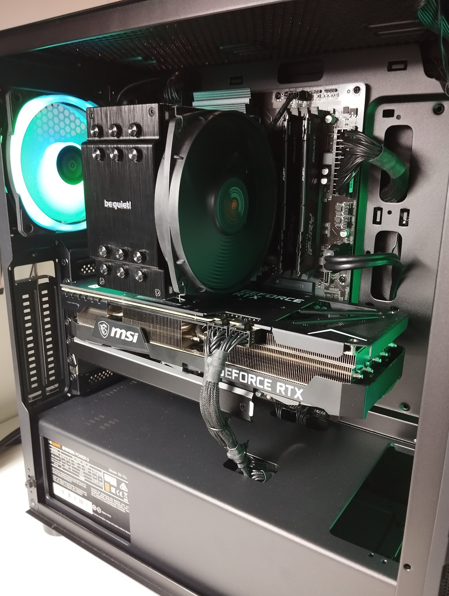 Wnętrze komputera stacjonarnego z kartą graficzną MSI GeForce RTX, chłodzeniem Be Quiet i pamięcią RAM Fury, podświetlone na zielono i niebiesko.