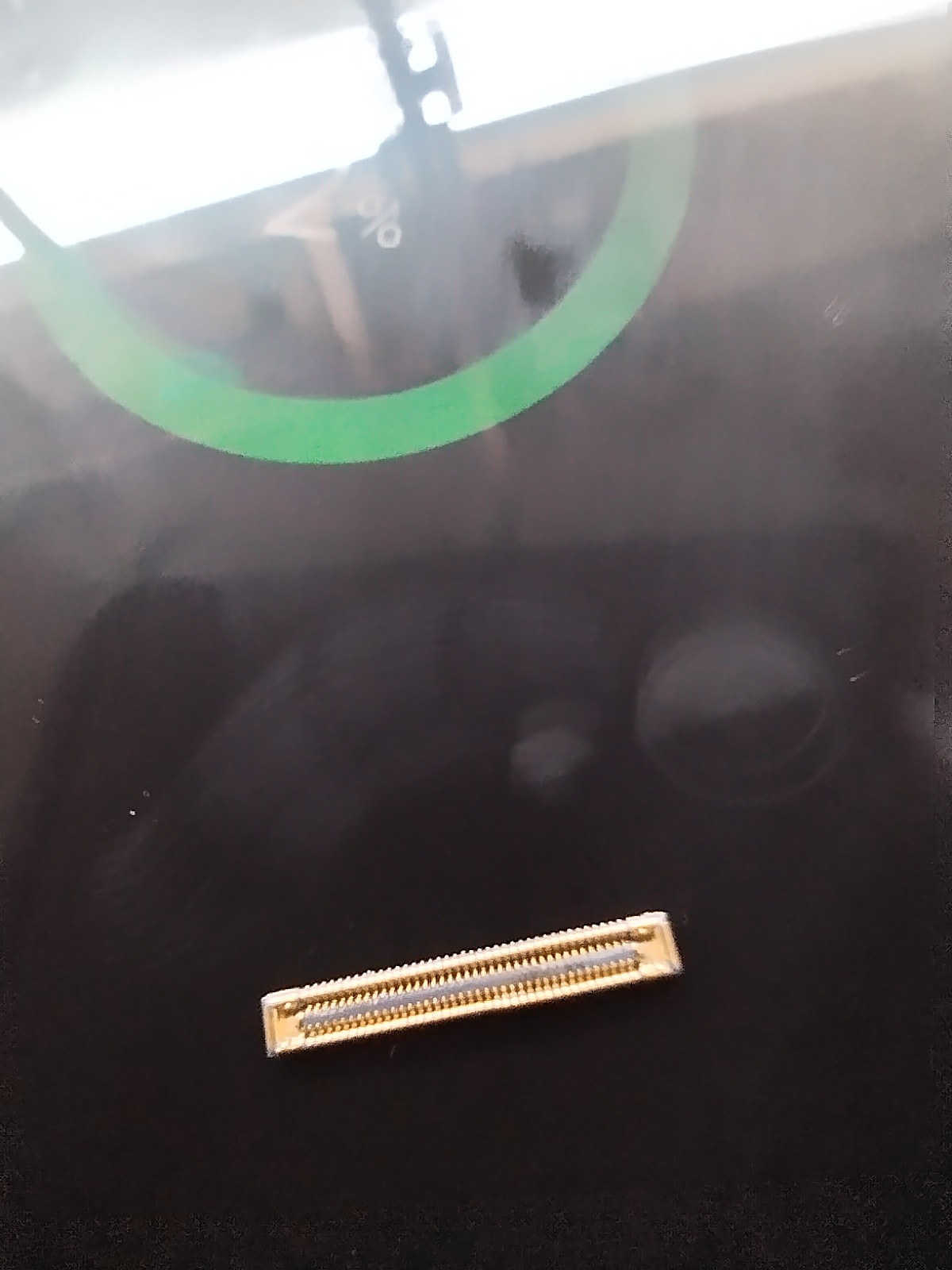 Złącze na płycie głównej laptopa, widoczne styki. Element naprawy komputera, prawdopodobnie po wymianie. Zielony okrąg w tle sugeruje trwający proces.