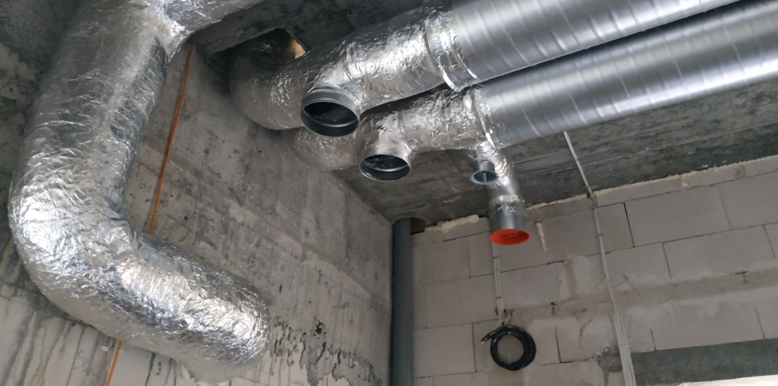 Instalacja wentylacyjna z izolowanymi przewodami aluminiowymi w surowym wnętrzu budynku z betonowymi ścianami i stropem.