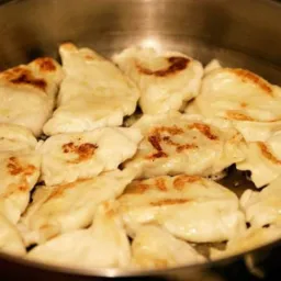 Smażone pierogi z delikatnym brązowieniem w dużej, metalowej patelni.