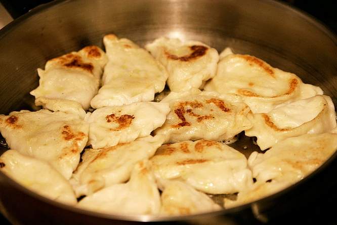 Smażone pierogi z delikatnym brązowieniem w dużej, metalowej patelni.