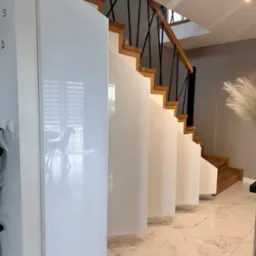 Nowoczesne schody z drewnianymi stopniami i czarnymi balustradami, zabudowane od dołu białymi, lakierowanymi panelami, marmurowa podłoga.