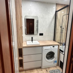 Meble Rostkowski - Nowoczesna łazienka w Małkini z zabudową meblową na wymiar, obejmującą szafki z szufladami, umywalkę nablatową, pralkę oraz lustro z podświetleniem, wszystko w jasnej kolorystyce z drewnianymi...