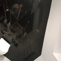 Błyszcząca, czarna podłoga w łazience z białymi żyłkami, odbijająca sufit z oświetleniem i osobę robiącą zdjęcie.