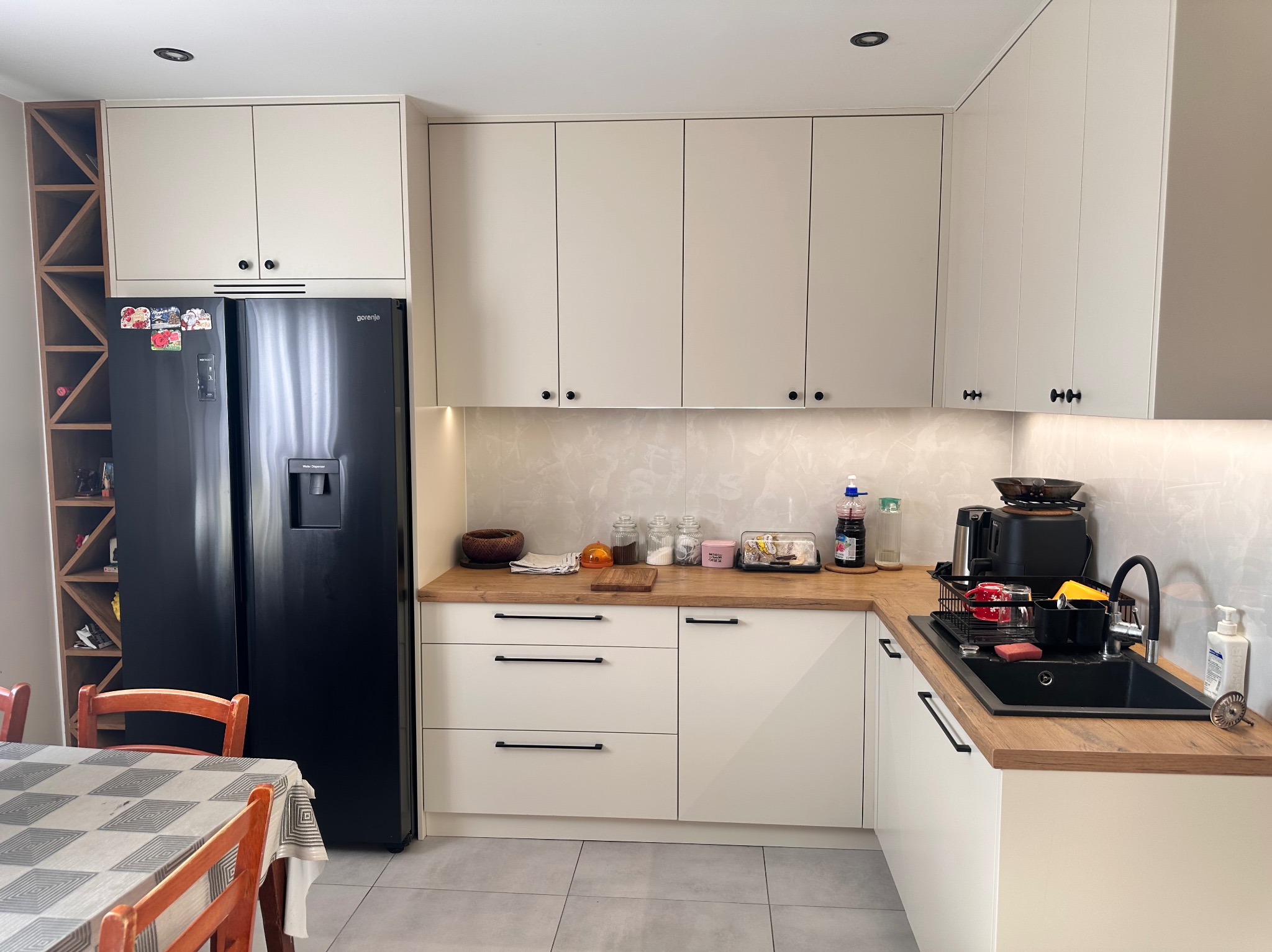 Jasna kuchnia z drewnianym blatem w Małkini z czarną lodówką i minimalistycznymi uchwytami szafek.