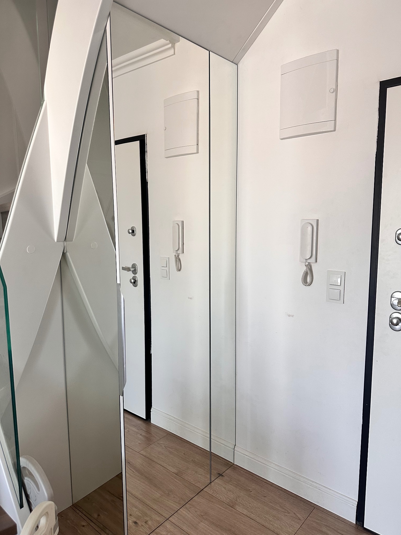 Wnęka z lustrzanymi drzwiami przesuwnymi, białe ściany z osprzętem elektrycznym i drewniana podłoga.