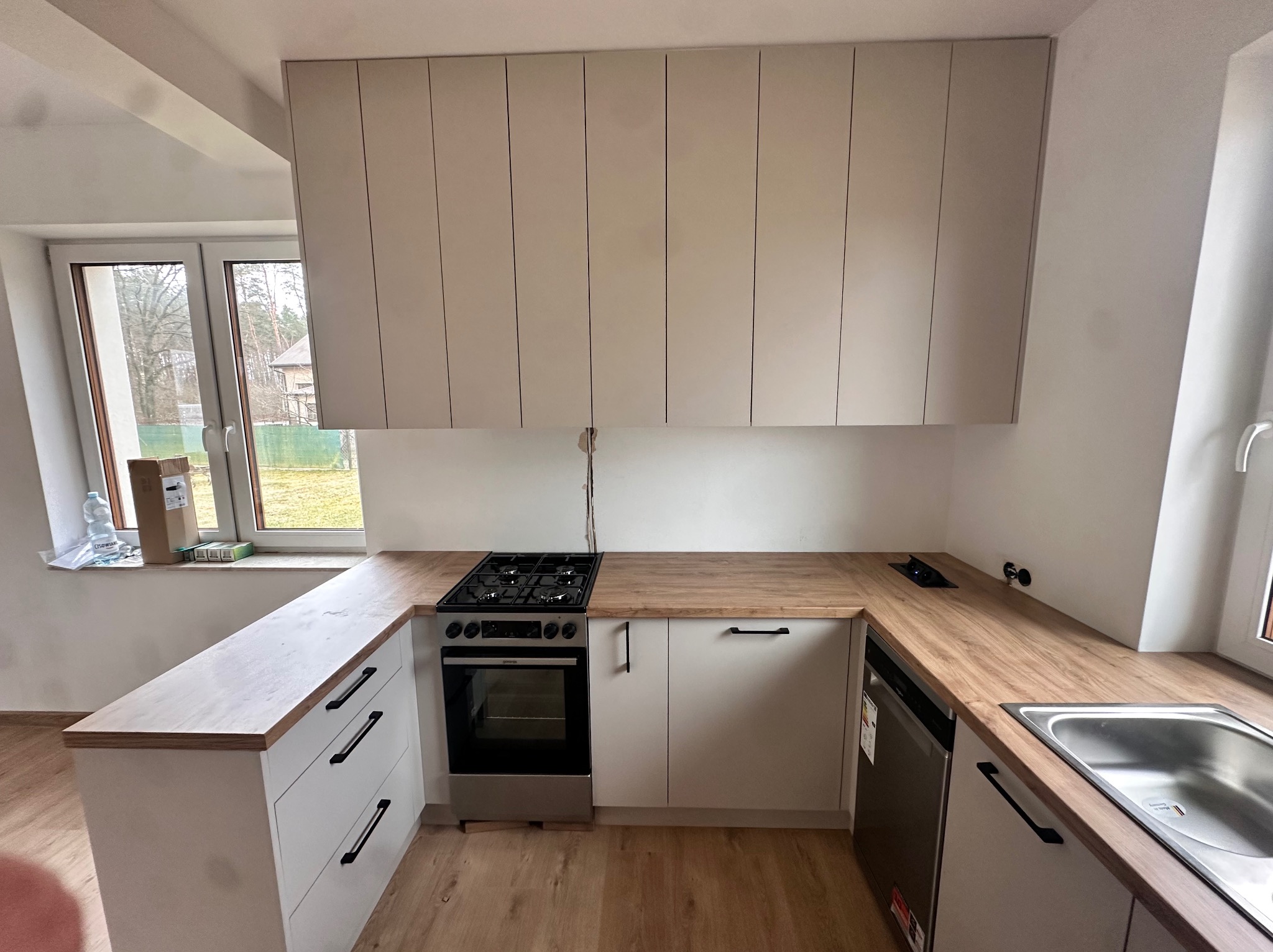Jasna kuchnia z drewnianym blatem i białymi szafkami, widoczny fragment okna i zabudowy kuchennej z piekarnikiem i płytą gazową.