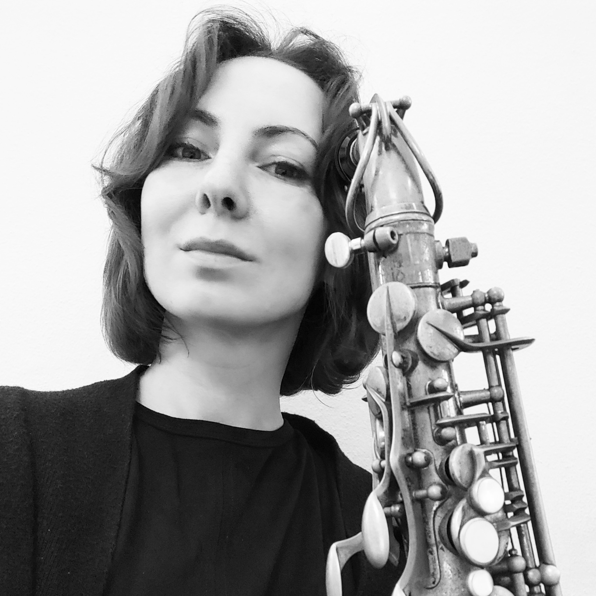 Portret kobiety w czerni z saksofonem w stylu vintage w czarno-białej tonacji, z widocznymi detalami instrumentu i wyrazem twarzy.