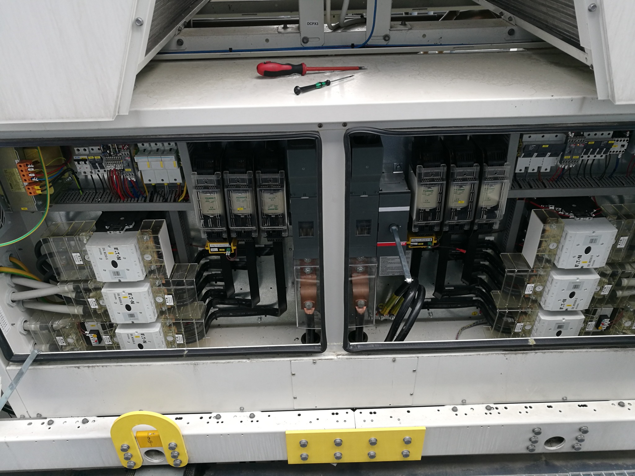 Otwarta szafa sterownicza z widocznymi stycznikami, bezpiecznikami i okablowaniem; na górze leżą dwa śrubokręty.