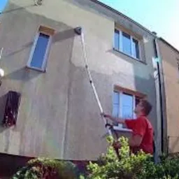 Czyszczenie elewacji domu jednorodzinnego z użyciem lancy teleskopowej, widoczna drabina oparta o ścianę budynku.