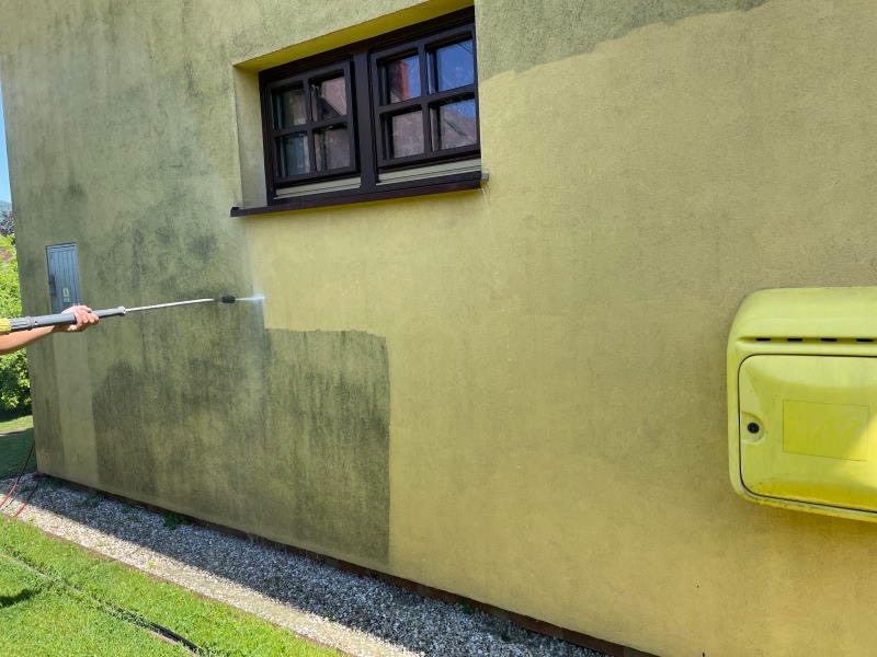 Czyszczenie elewacji myjką ciśnieniową w Nowym Dworze Mazowieckim, widoczna różnica między umytą a brudną powierzchnią, żółta skrzynka gazowa na ścianie.
